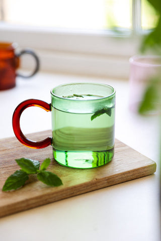 A green glass mug with a deep red handle. 