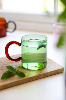 A green glass mug with a deep red handle. 