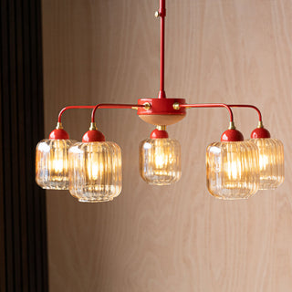 Lifestyle image of the Rockett St George Red Metal & Ribbed Glass Ceiling Light illuminated and hanging in front of a wooden wall. 