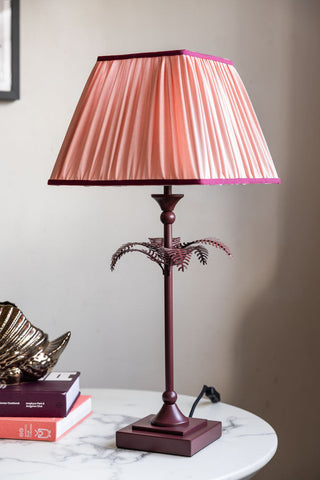 A pink and burgundy table lamp with a palm tree on the base. 