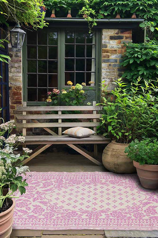 Pretty garden patio with pink rug, lots of green plants and a garden bench