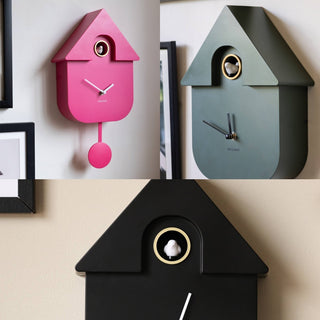 A picture of three modern cuckoo clocks, one pink, one black and one khaki 
