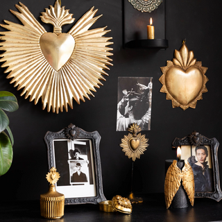 A stunning dark wall decorated with gold milagro hearts, candlesticks and candle holders.