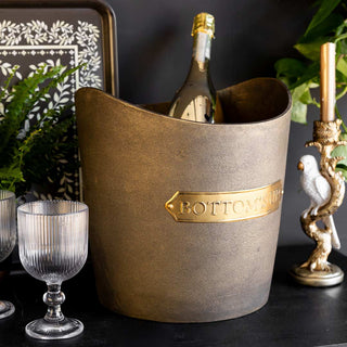 The Bottoms Up Champagne Bucket styled with a bottle inside, displayed on a sideboard with glassware, greenery, a tray and parrot candlestick holder.