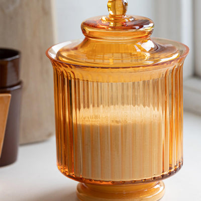 An orange glass storage jar styled with some sugar inside, styled on a kitchen worktop with a window and some accessories in the background.