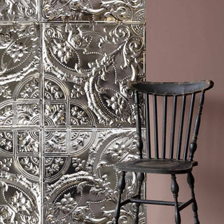 The  Filigree Tin Tiles displayed on a pink wall behind a wooden chair.