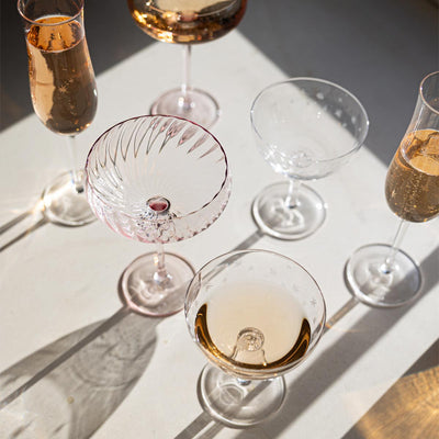 Various champagne/cocktail glasses styled on a white table in the sun.