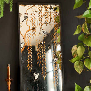 The Weeping Willow Tree & Bird Mirror displayed leaning against a black wall, with a candlestick holder and plants.