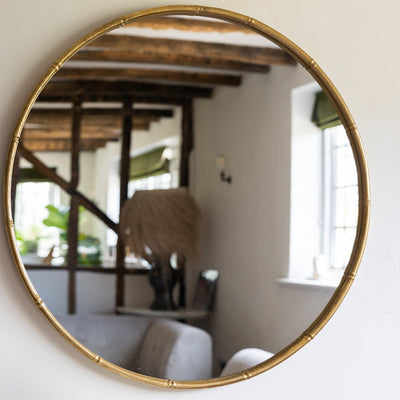 Lifestyle image of the Rockett St George Round Antique Gold Wall Mirror displayed on a neutral wall. 