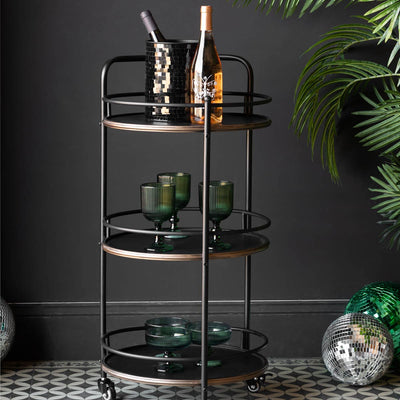 A metal drinks trolley styled with various bar accessories on, next to a plant and disco ball in front of a black wall.