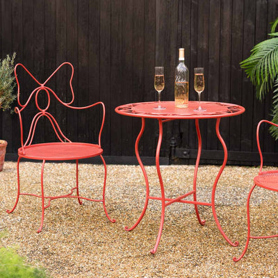A red bow garden furniture set styled oudoors on a patio are with some glasses, a bottle and some plants.
