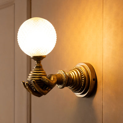 A gold flower wall light switched on and displayed on a plain wall.