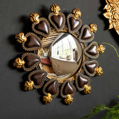 A round mirror with heart shaped details displayed on a black wall.