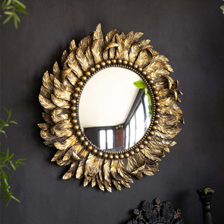 Lifestyle image of the Rockett St George Golden Feather Round Wall Mirror displayed on a black wall accompanied by another mirror, plant and candlestick holder. 