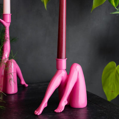 A colourful gold candlestick holder with two love bird figures on, styled with some lit candles on a table with a plate and a cocktail glass.