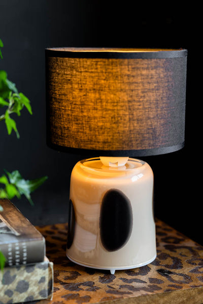 A black cordless table lamp styled on a round table with a pair of glasses, a mug and a magazine.