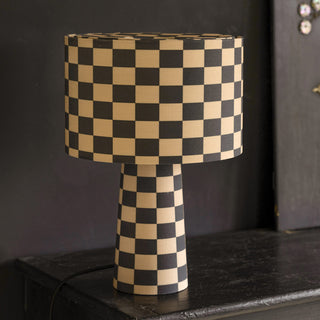 The Charcoal & Natural Checkerboard Table Lamp displayed on a black sideboard in front of a black wall.