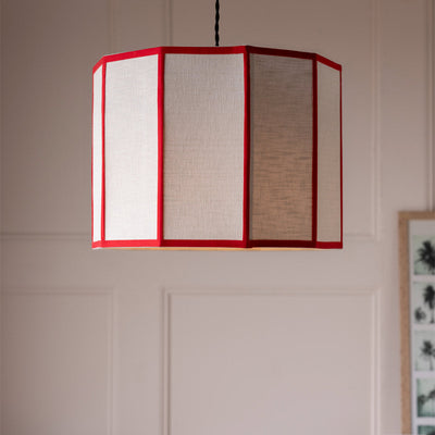 A red contrast linen lampshade hanging in front of a white panelled wall.
