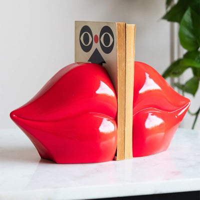The Bold Red Lips Bookends styled on a marble surface with some books, with a plant in the background.