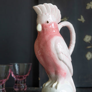 The Pink Cockatoo Carafe Jug displayed on a black table with pink glassware in the background.