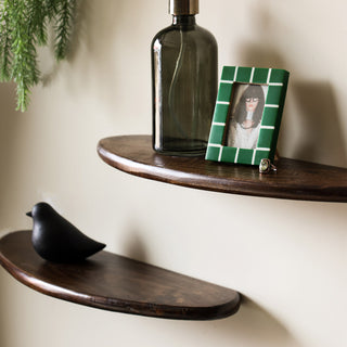 The Set Of 2 Walnut Wood Floating Shelves on the wall displayed with various home accessories and a plant.