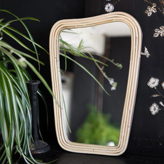 Lifestyle image of the Small Abstract Rectangle Bamboo Wall Mirror displayed in front of a black wall with a black candlestick holder, plant and floral decoration.