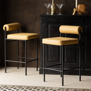 Two of the Sand Faux Leather Roll Back Bar Stools displayed in front of a black sideboard styled with various glassware and home accessories.