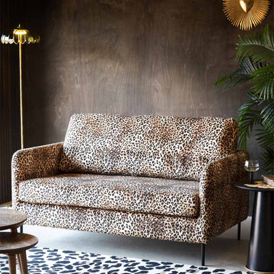 Image of a leopard print sofa styled with a floor lamp and various accessories in front of a dark wall.