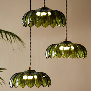 Lifestyle image of the Palm Cluster Light illuminated, in front of a neutral wall with a plant in the background. 