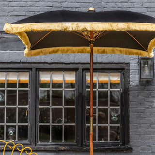 Lifestyle image of the Rockett St George Black Square Printed Parasol styled in front of a window of a black brick building. 