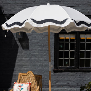 The HKliving Vintage Flower Parasol displayed in front of a black tiled building with a chair and cushion, a plant and greenery.