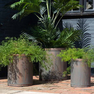 The Set Of 3 Antique Copper Garden Tub Planters displayed on a brick patio with various plants inside.
