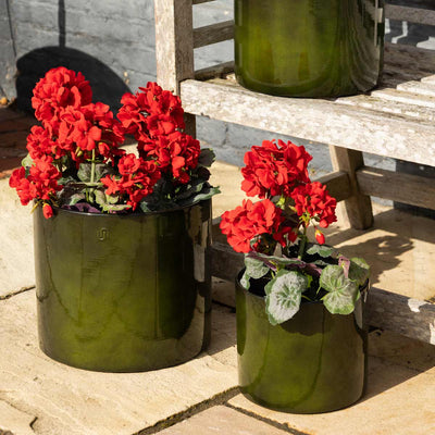 Some outdoor green plant pots styled on a patio with red flowers inside.