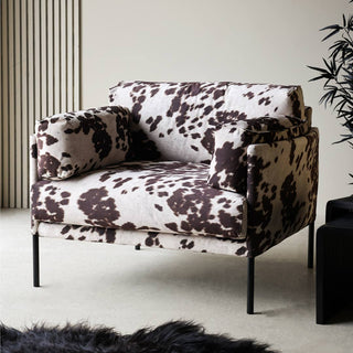 Lifestyle image of the Rockett St George Cowhide Patterned Armchair styled in a neutral room with a rug, nest of tables and plant. 