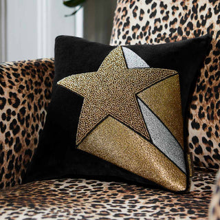 The Black Geo Bolster Cushion displayed on a yellow sofa, with a table lamp in the background.