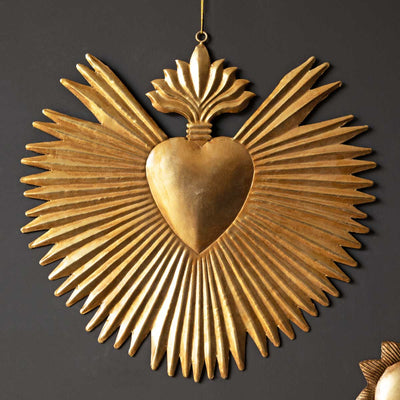 A gold milagro heart ornament hanging on a dark wall.