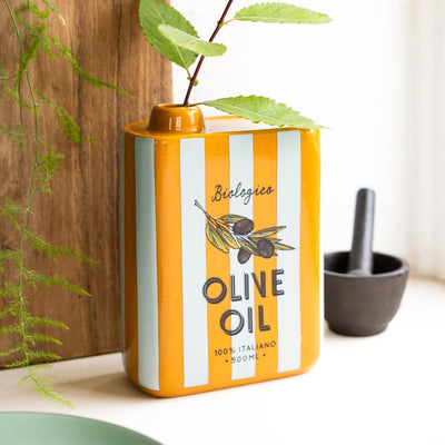 A striped vase in the styled of an olive oil bottle, styled with some greenery and a pestle and mortar.