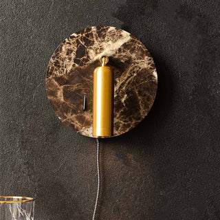 Lifestyle image of the Rockett St George Marble Effect Wall Light With USB Phone Charger displayed on a black wall and styled with a gold rimmed glass on a table beneath. 