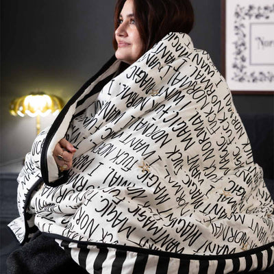 A monochrome printed blanket wrapped around a model, with a lamp switched on in the background.