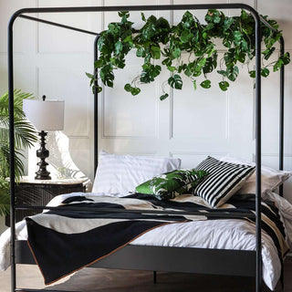 The Black Metal Four-Poster Bed - King Size in a bedroom, styled with various home accessories and greenery.