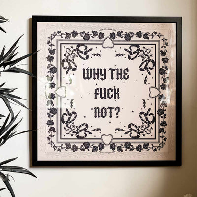 A framed art print that says 'why the fuck not?'. displayed on the wall next to a plant.