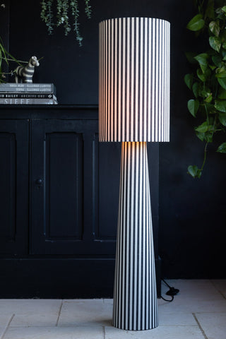 Black and white striped floor lamp lit in a dark living room setting.
