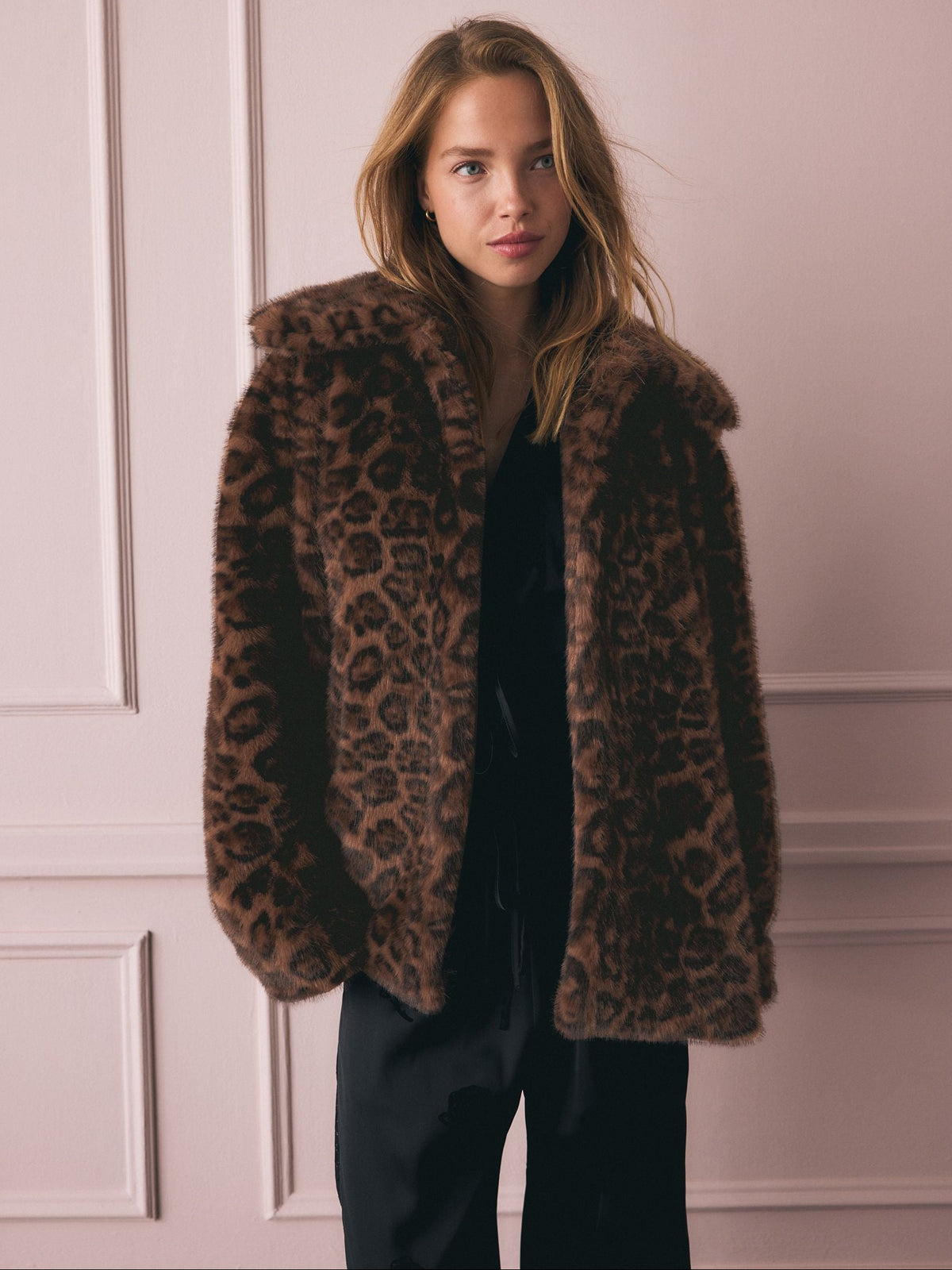 Woman wearing a leopard print coat against a light pink wall.