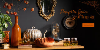 A styled Halloween-themed tabletop scene with orange and gold pumpkins, a tall amber vase with dried flowers, a glass cloche, two glasses of amber drink, and decorative wall art against a dark wall. Text on the right reads 'Pumpkin Spice & All Things Nice' with a 'Shop Halloween' button.