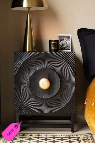 The Circular Ribbed Wood Detail Bedside Table styled with a lamp, candle and photograph on, next to a bed.