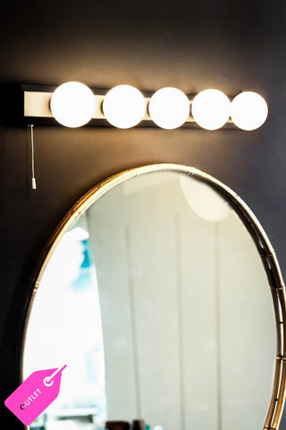 The Hollywood Vanity Wall Light in Black styled on a dark wall above a round mirror.