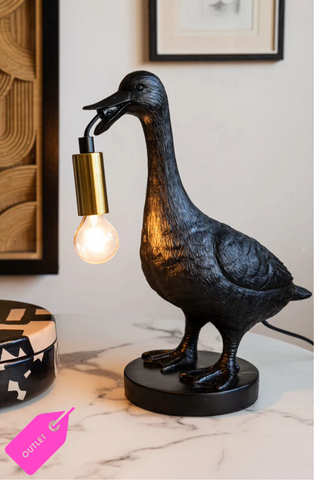 Lifestyle image of the Duck Table Lamp on a marble surface with a picture on the wall behind it.