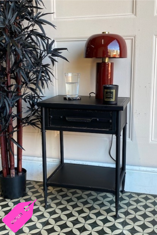 Image of Black Metal Industrial Style Bedside Table with a dark red lam on the surface on a black & white floor