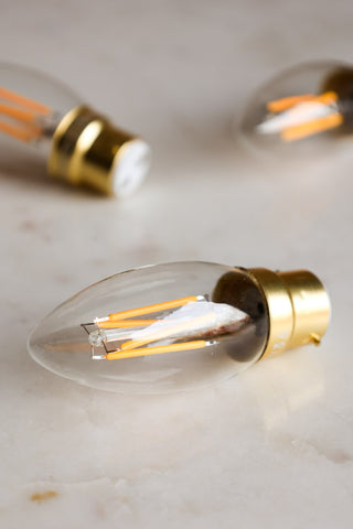 Lifestyle image of multiple Candle B22 4W Clear LED Light Bulbs on a white marble surface. 