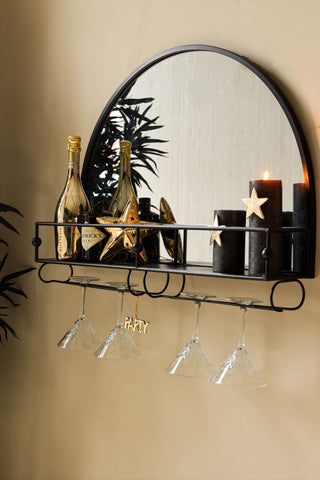 Lifestyle image of wall mounted black metal bar shelf with mirror against a plain wall, styled with kitchen accessories, candles and a plant. 